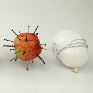 A red apple with nails stuck in it next to a white pebble wrapped in cord