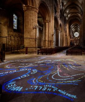 Text is projected in light onto the sandstone floor of Durham Cathedral 