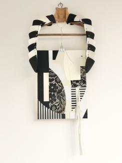 A vintage coat hanger draped in multiple shoulder pads with a collage suspended beneath. 