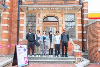 Six students standing on a step outside the front door of Dora House, the home of the Royal Society of Sculptors