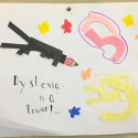 Poster with text 'Dyslexia is Power' with an image of a black rocket and abstract pink and yellow shapes