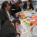 Image shows four students in black and red school uniform writing on large paper together