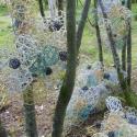 Sculpture made with wire and packaging, sited among trees.