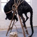 An over-sized cat is seen climbing over a ladder, but someone has tied it down with a large coil of rope